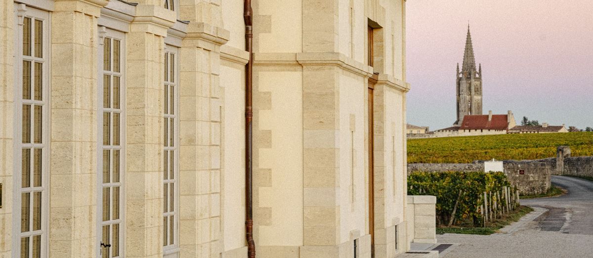 Außenaufnahme von Château Beau Séjour Bécot, im Hintergrund auf der rechten Seite sind die Weinberge und ein Kirchturm erkennbar.