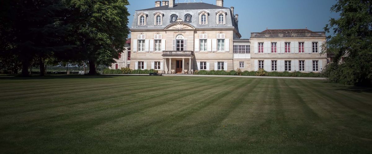 Blick über eine freie grüne gemähte Wiese mit Bäumen am Rand auf Chateau Pontet-Canet.