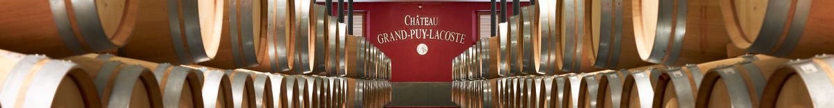 Weinkeller von Château Grand Puy-Lacoste mit aufgereihten Weinfässern links und rechts und dem Logo des Château in der Mitte am Ende eines Flurs.