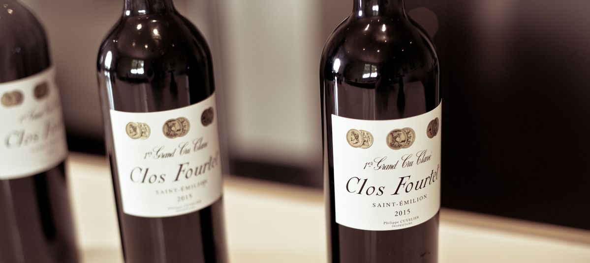 Drei Weinflaschen von Chateau Clos Fourtet stehen aneinandergereiht auf einem weißen Tisch