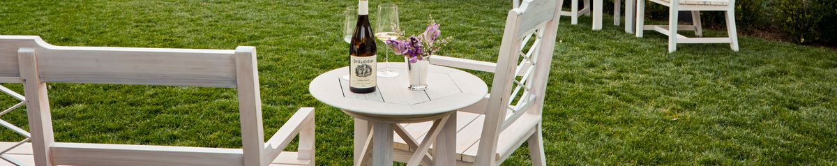 Eine Weinflasche von Weingut Heitz steht auf einem weißen Holztisch mit weißen Stühlen und Blumendeko.