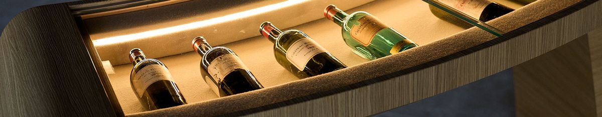 Mehrere Weinflaschen-Jahrgängen von Château Haut-Bailly liegen in einer kurvigen Vitrine und werden von indirektem Licht angeleuchtet.