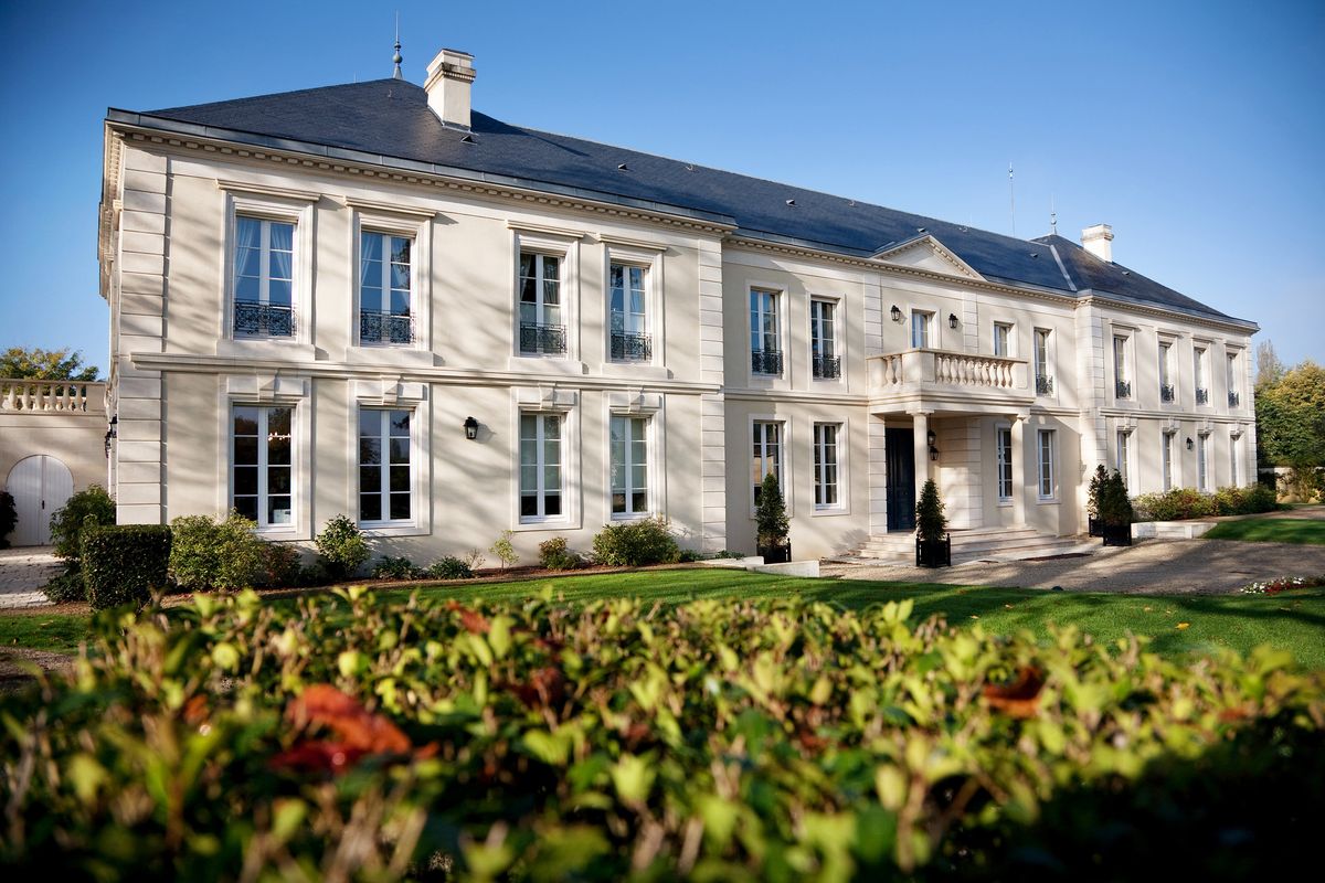 Weißes Haus von Chateau Malartic Lagraviere unter blauem Himmel hinter Weinreben