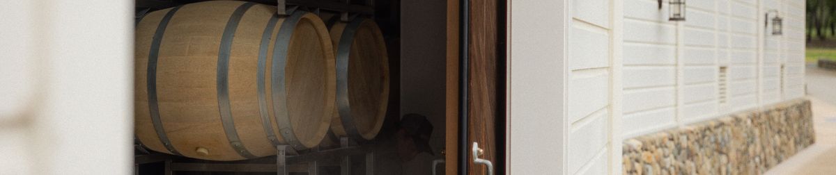 Blick seitlich in den Weinkeller auf gelagerte Weinfässer bei geöffneter Tür auf Peter Michael Winery