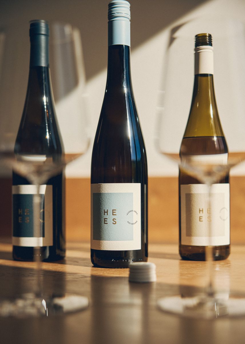 Drei Weinflaschen von Weingut Hees stehen im Hintergrund mit geöffneten Schraubverschlüssen und Weingläsern im Vordergrund