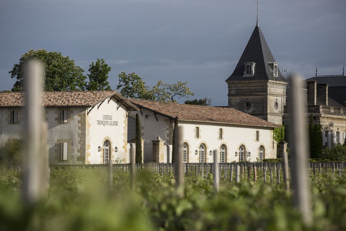 Weißes Gebäude mit roten Dachziegeln und grauem Steinturm hinter Weinreben von Chateau Tronquoy Lalande