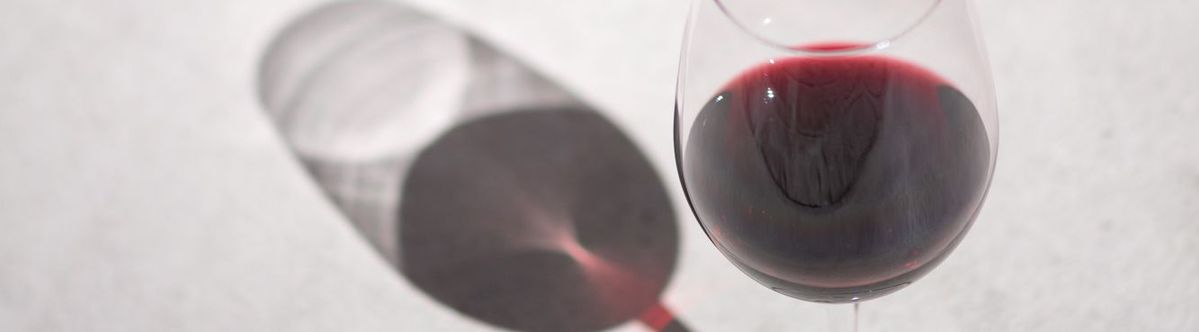 Ein gefülltes Rotweinglas mit einem Wein von Château Berliquet steht in der Sonne und wirft einen Schatten