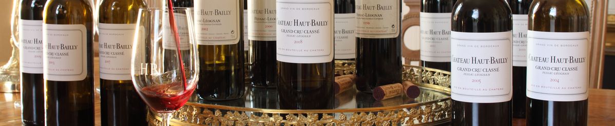 Viele verschiedene Jahrgänge von Château Haut-Bailly stehen auf einem Tisch. In ein Weinglas im Vordergrund wird Rotwein eingeschenkt.