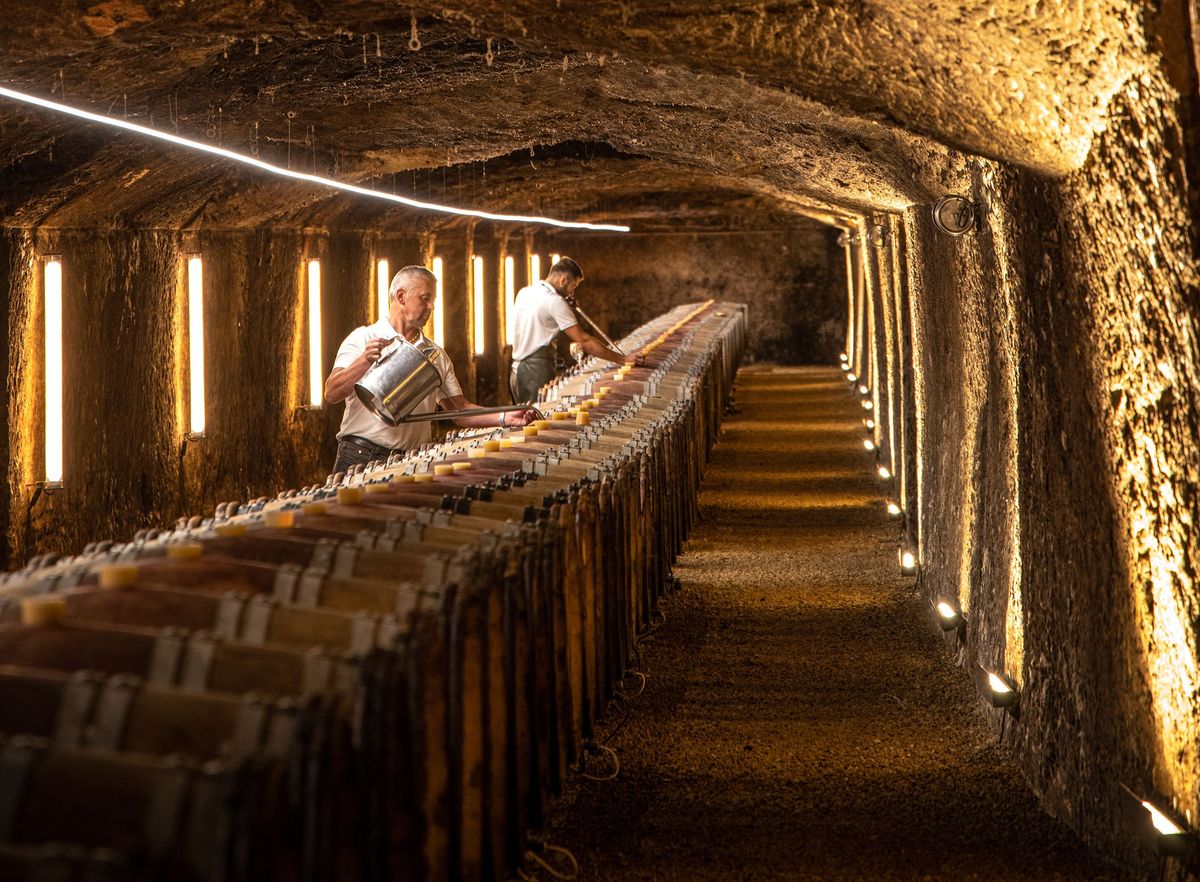 Aneinanderliegende Holzweinfässer von Chateau Clos Rougeard in dunklem Steinkeller mit zwei Männern
