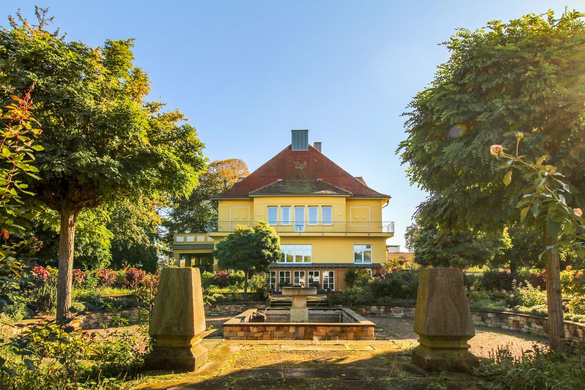Villa von Sekthaus Raumland unter blauem Himmel mit gelben Haus und Garten umgeben