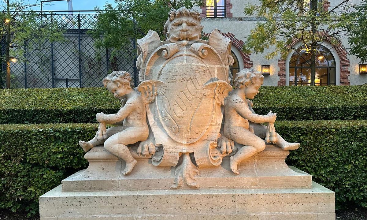 Steinstatue von zwei Engeln neben Wappen von Moet et Chandon vor weißem Gebäude