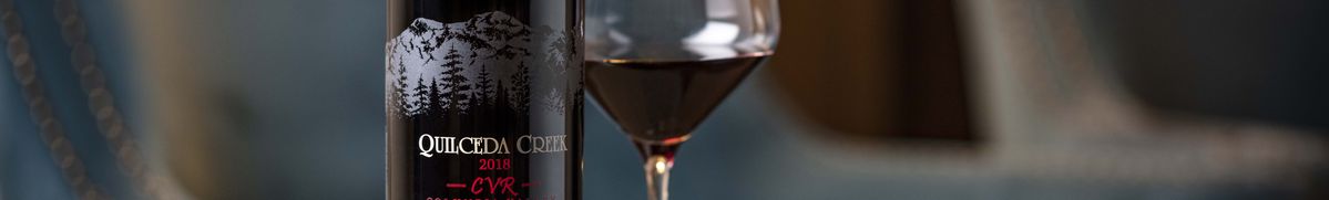 Nahaufnahme des Etiketts von einer Weinflasche des Weinguts Quilceda Creek, daneben ein gefülltes Glas Rotwein.
