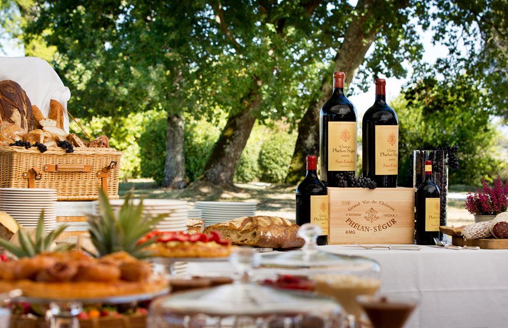 Gedeckter Picknick Tisch mit Garten im Hintergrund und Weinflaschen von Chateau Phelan Segur darauf
