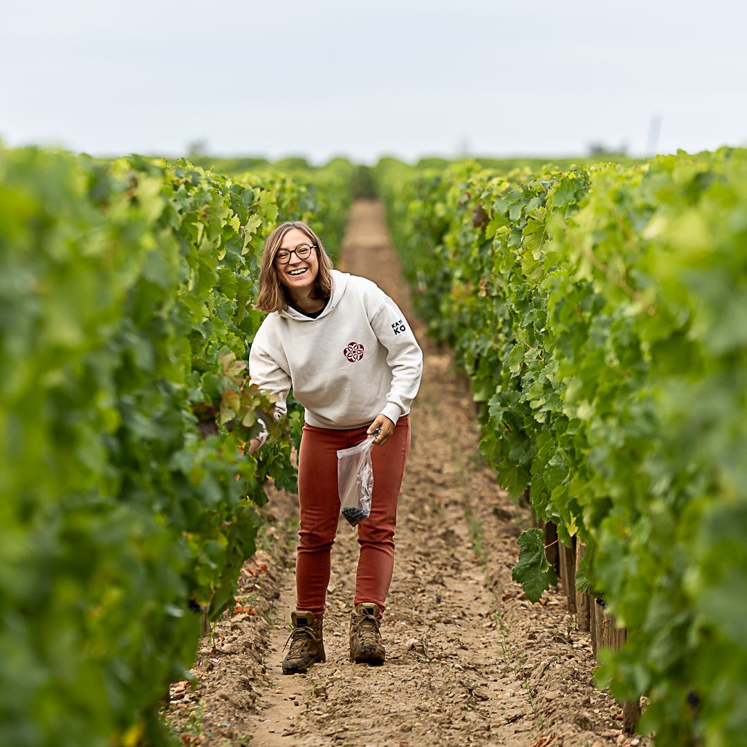 Frau mit grauem Pulli und roter Hose steht in der Mitte von Weinreben von Chateau Lafleur