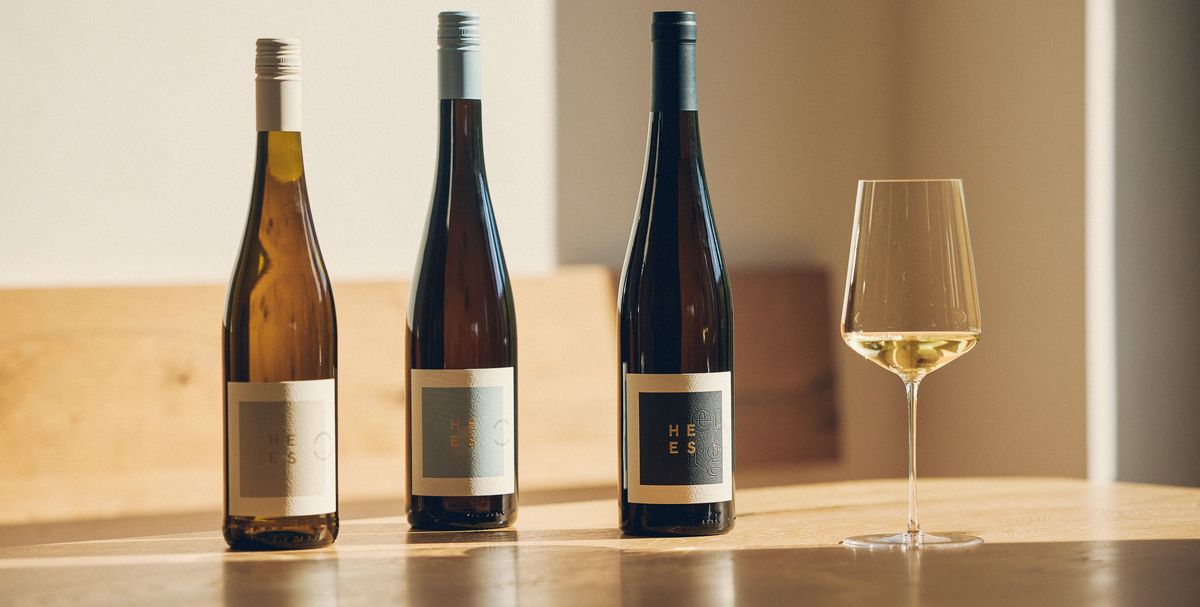 Drei Weinflaschen vom Weingut Hees mit gefülltem Weinglas stehen im Sonnenlicht auf einem Holztisch