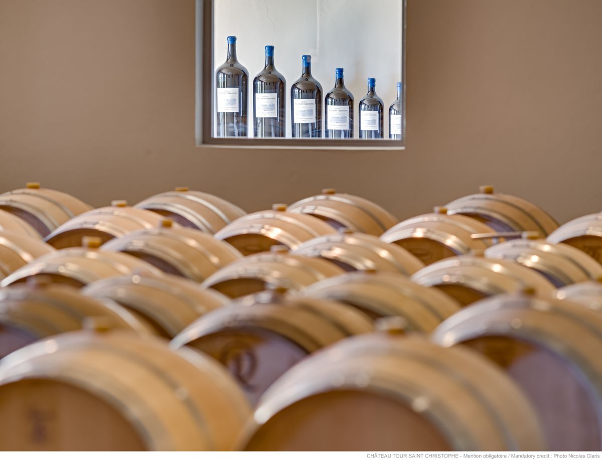 Holzweinfässer von Chateau Tour Saint Christophe im Vordergrund mit Ausstellfenster mit sechs Flaschen Wein