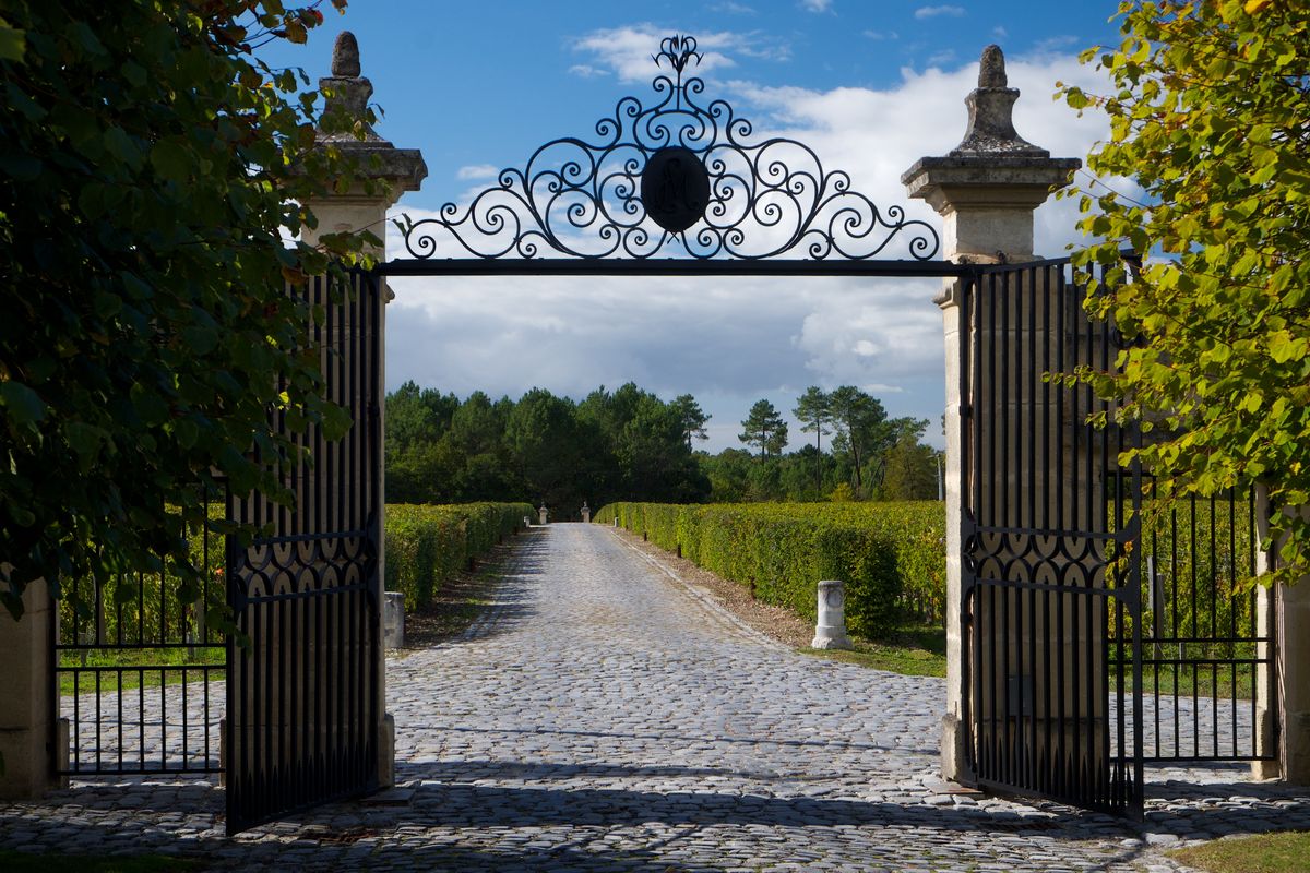 Stahltor mit Steinstraße vor Weinreben von Chateau Giscours unter blauem Himmel