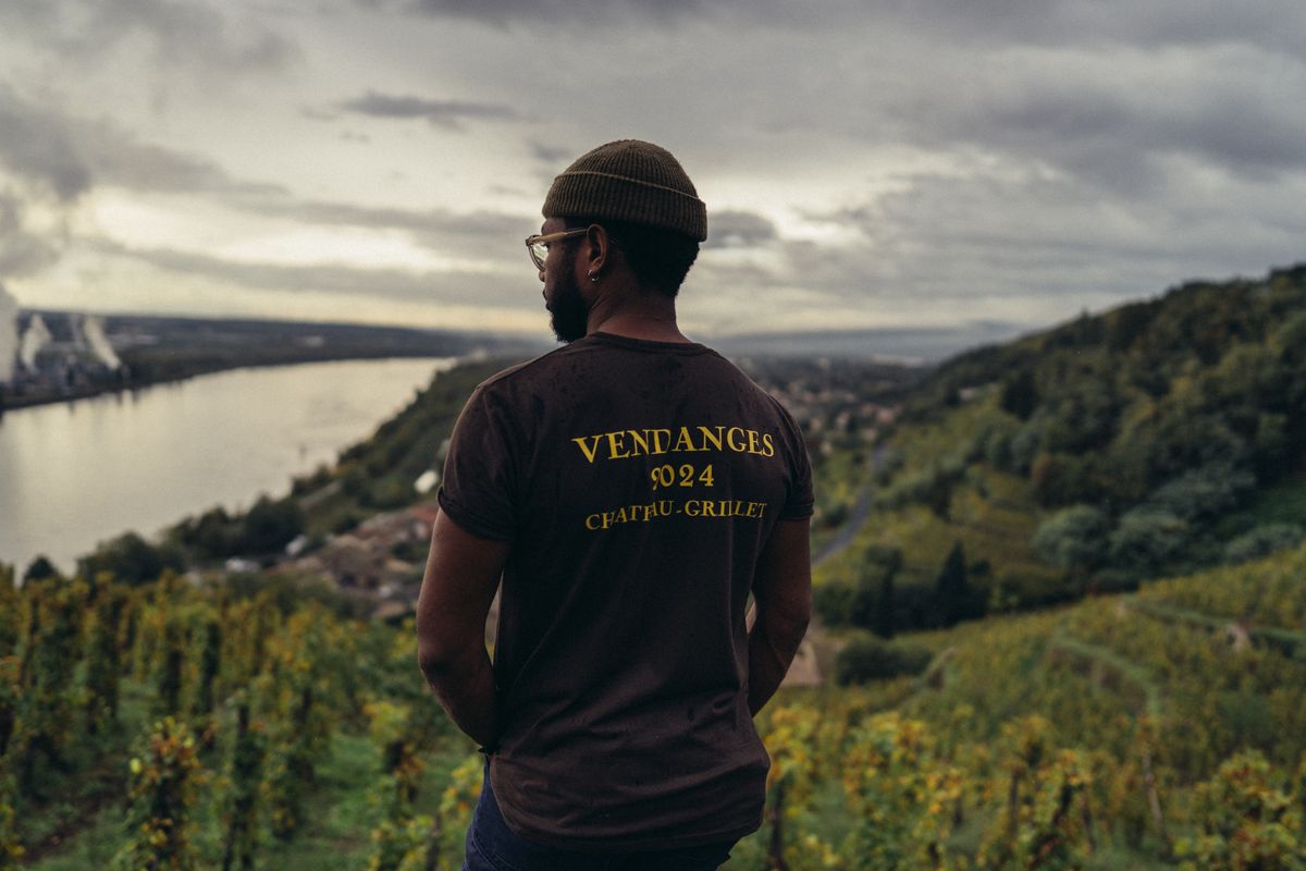 Mann steht mit den Rücken zur Kamera im Hintergrund Weinberge von Chateau Grillet unter grauem Himmel und neben Fluss