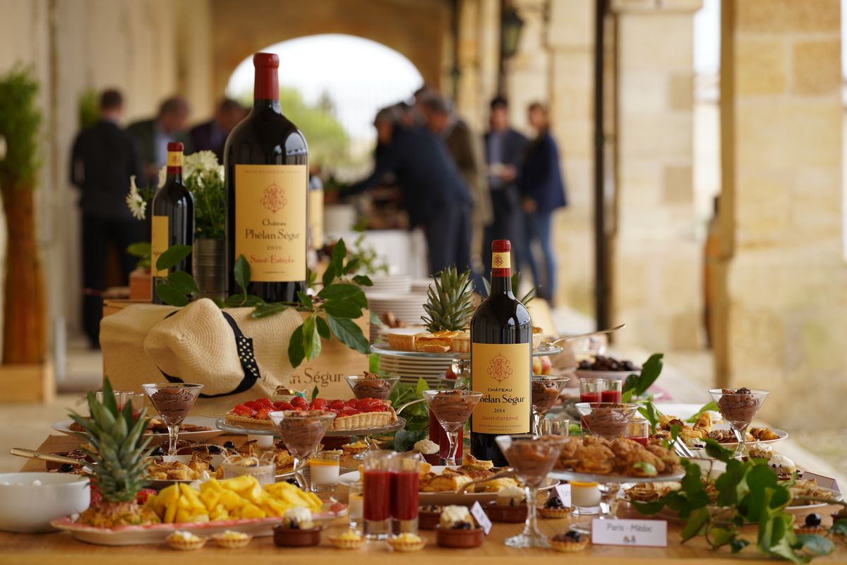 Gedecketer Tisch mit viel Essen und zwei Weinflaschen von Chateau Phelan Segur mit Personen im Hintergrund