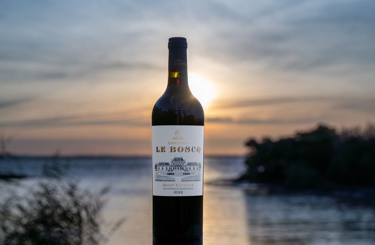 Weinflasche von Chateau Le Boscq stehend vor einem See mit Sonnenuntergang im Hintergrund